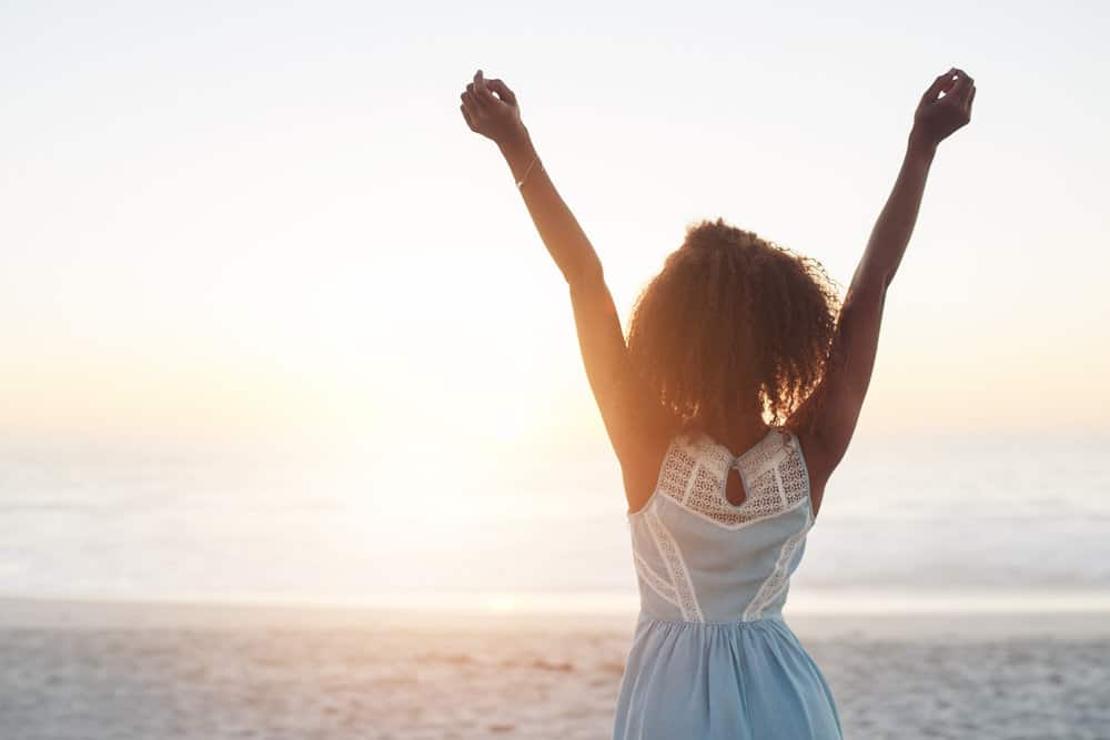 A confident, happy black female that experienced hair shedding is walking on the beach.