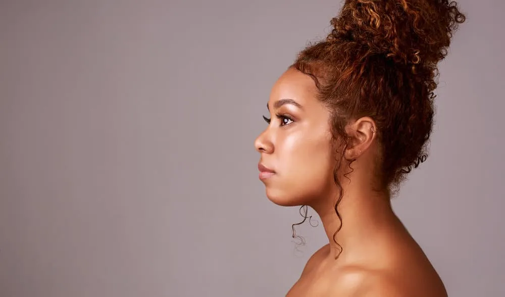 9 Easy Curly Hair Updos: How to Create Curly Updo Hairstyles 18 A gorgeous image of a black female with shoulder-length curly hair showcases her natural texture in a loose bun with a few fresh flowers, creating an effortless and beautiful style.