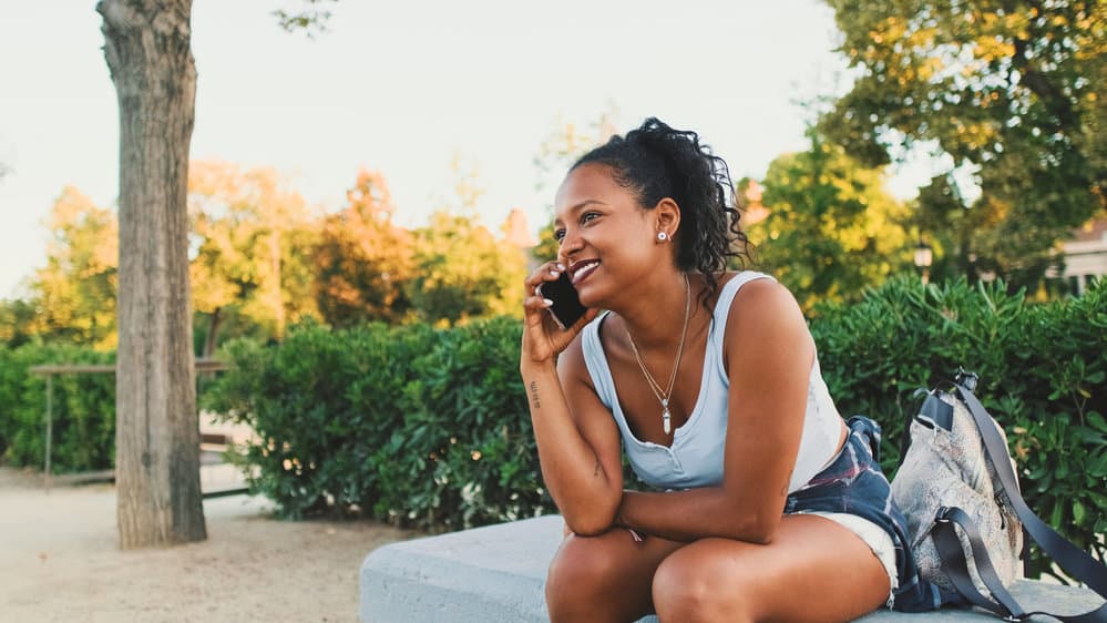 A beautiful African female asks a friend are hair growth vitamins safe during a phone call.