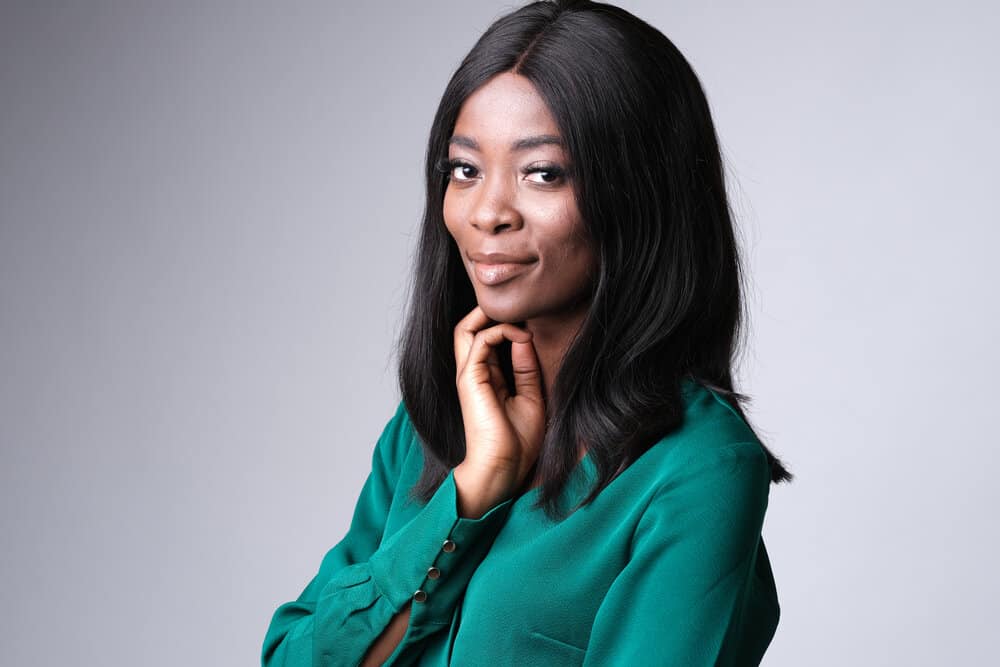 A cheerful young African American female wearing a lace front wig with a stylish green dress.