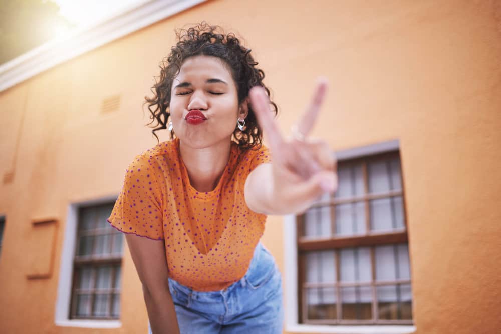 A black female is showing a peace sign with her fingers after posing with different hair styles.