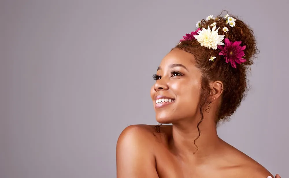 9 Easy Curly Hair Updos: How to Create Curly Updo Hairstyles 14 A black female with curly tresses showcases her hair type in a curly top knot, styled with a hair tie and a few bobby pins to keep it in place.