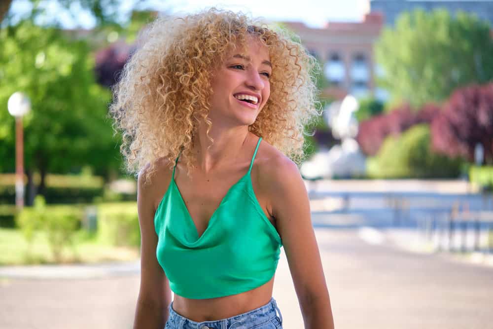 A young Brazilian woman wearing medium smokey ash-blonde curls toned with 7A medium liquid toner.