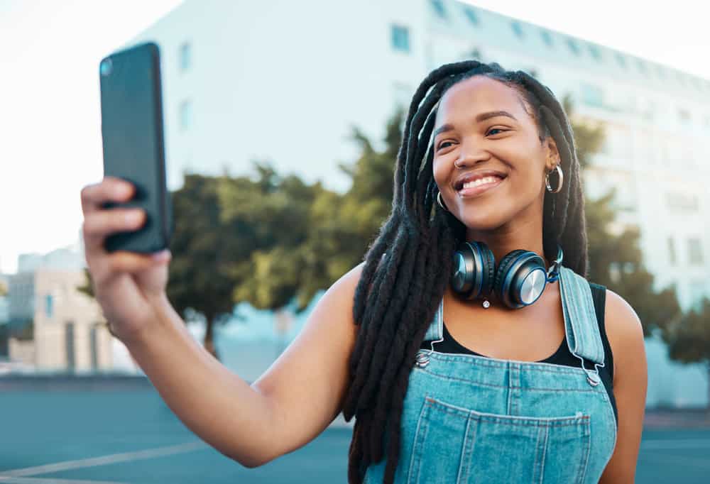 A young African American female takes a selfie after discussing how to start locs on wavy hair with a friend.