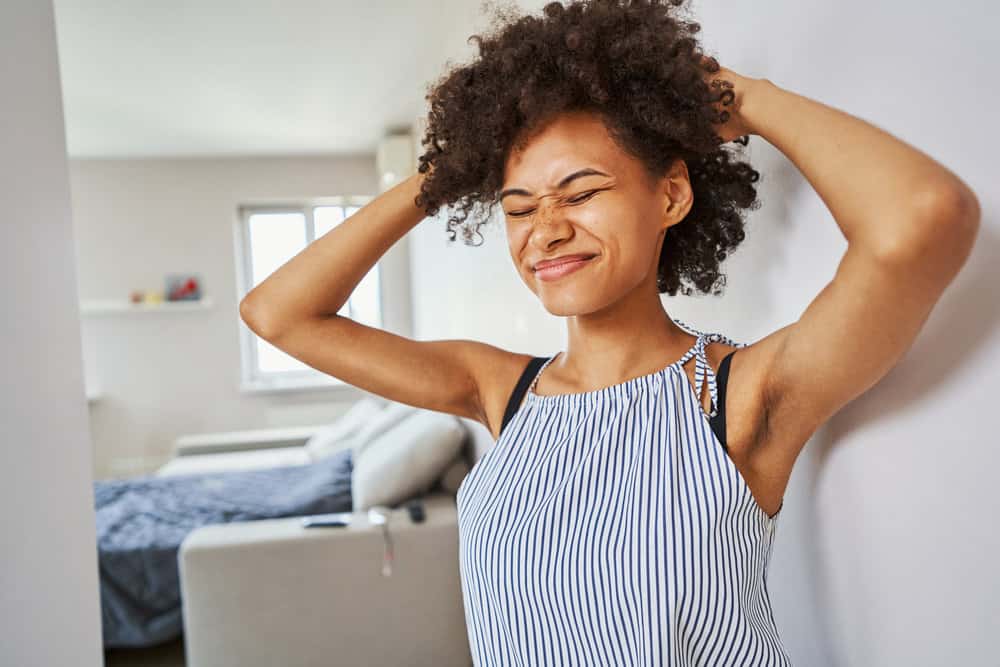 A black girl uses an ouchless hair tie to gently scrunch her natural curls.