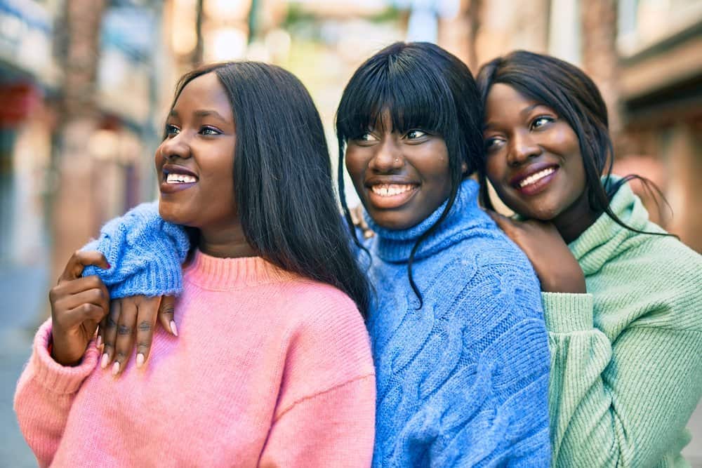 Three cousins wearing synthetic lace front wigs are outdoors taking photos after meeting for lunch on a spring day.