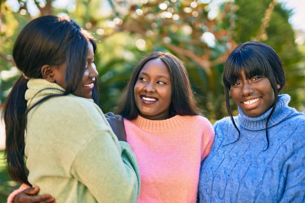 Three friends in a local park wearing curly lace wigs made from synthetic hair.