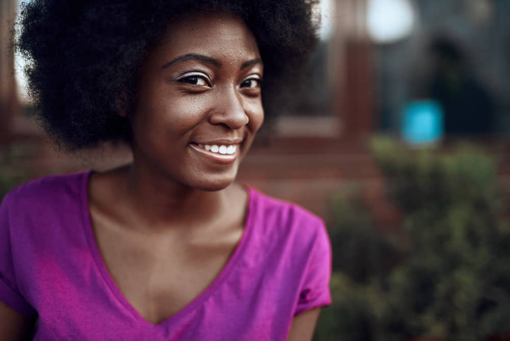 A cute young black girl with a defined curl pattern has natural hair shrinkage on her 4C hair strands.