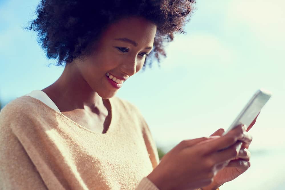 A black girl reading about hair health and dry hair prevention tips on her mobile phone.