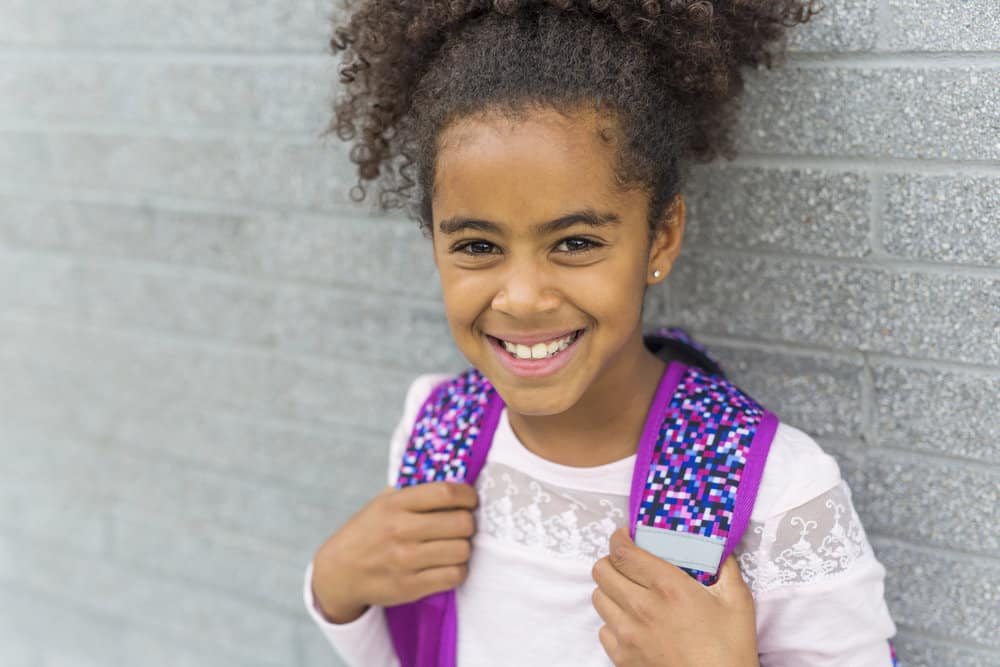 The cute little black girl's simple bun with curly ends is a low-maintenance hairstyle that allows her to express her unique style and personality.