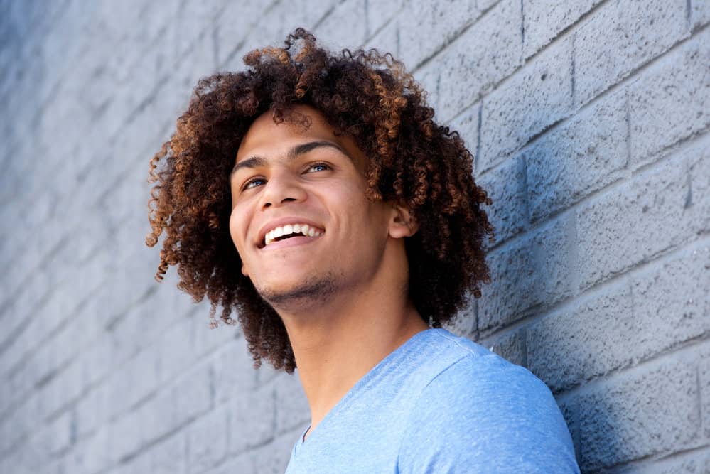 A man, with his long curly hair resembling a sea of natural waves, styled with the artistry of a tan and dark brown ombre.