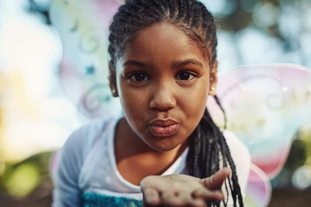 A little girl wearing a low maintenance kids box braids style with synthetic hair extensions added in to make her fine hair long enough for braids.