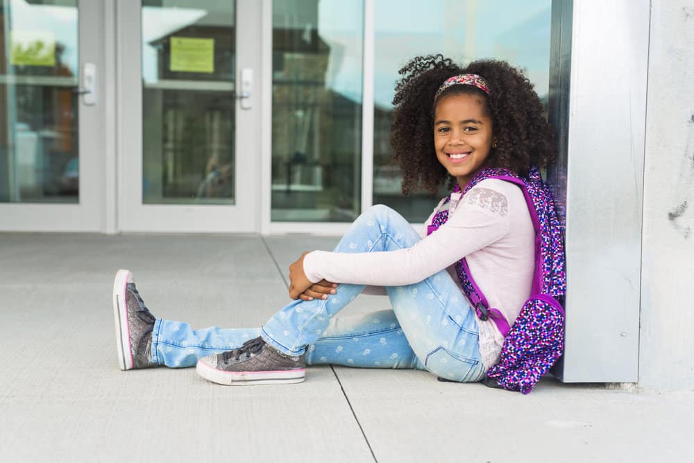 With her dark brown, thick hair styled in a simple bun with curly ends, the young black girl exudes confidence and charm.