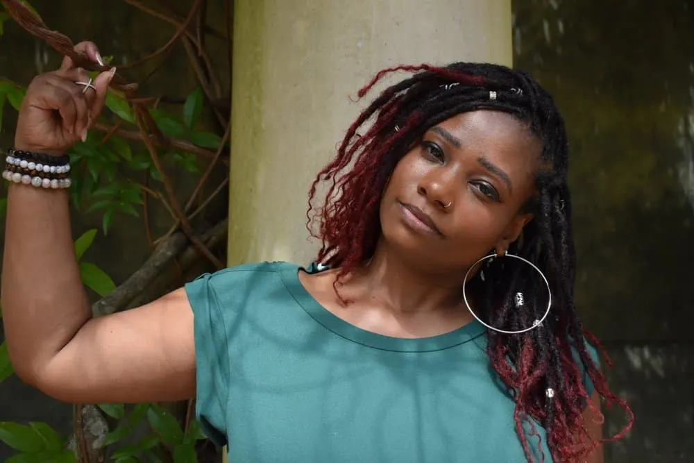 Butterfly Locs: How to Do Butterfly Loc Hairstyles at Home 1 A cute black girl with naturally curly, wavy hair stands wearing long butterfly locs in a protective style with her edges styled with edge control gel.