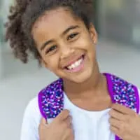 A cute young black girl with dark brown, thick hair in a simple bun with curly ends is wearing a classic style that her mom created with human hair extensions.