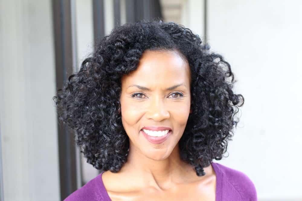 A mature black female with salt and pepper hair wears a chin length bob as gray hair strands start to peek through her black natural hair color, complimenting her slender facial features.  