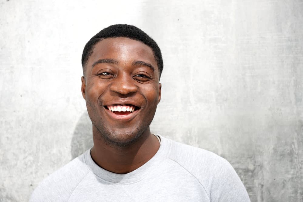 A black man wearing a modern high fade haircut on dark hair that requires very little effort each morning with hair on top of the head of this low maintenance hairstyle.