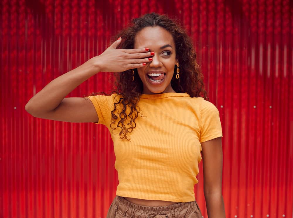 The pretty black woman embraces her natural curly hair, using natural oils to create a soaking wet hair appearance on her dark brown, thick locks.