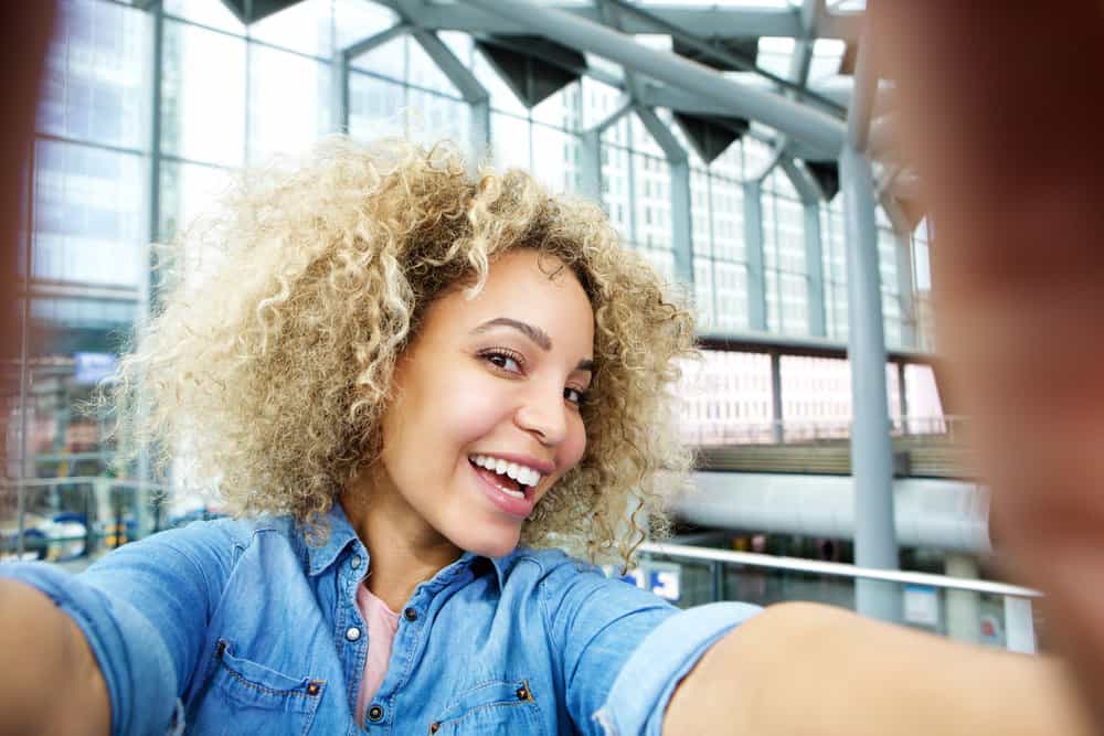 The pretty black woman confidently flaunts her blonde hair with light brown undertones, achieved through a professional hair bleach treatment by a skilled colorist.