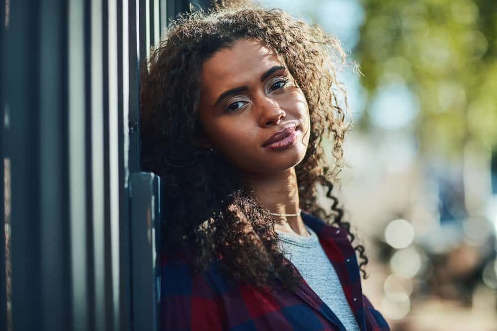 A beautiful black female with natural curls has frizzy hair after heat styling her bouncy curls with a blow dryer and frizz-control hair gel after washing with a sulfate-free shampoo.