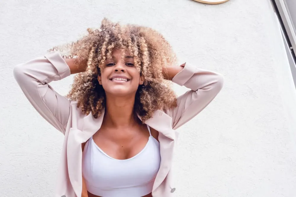 The fashionable young black woman rocks a stunning balayage look on her natural curl pattern, with beautiful blonde and brown hair strands enhancing her textured hair.