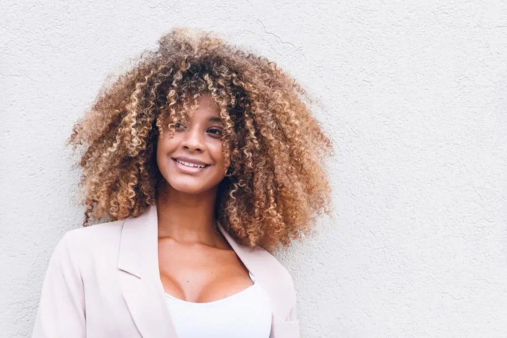 How to Brush Curly Hair Without Losing Curls or Frizzy Hair 1 A stunning black female with a type 3 curl pattern styled with natural oils has beautiful blonde and brown hair strands creating a cool balayage look on her natural curls.