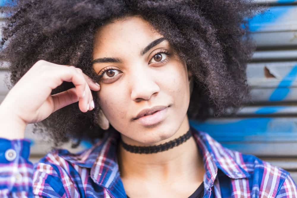 A beautiful black woman with natural curls after brushing curly hair with a Tangle Teezer to detangle her dry curly hair strands and highlight her loose curls.