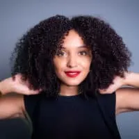 A beautiful black female with wavy hair used a leave-in conditioner and natural oils to highlight her natural texture and bring out her curly, fine hair.