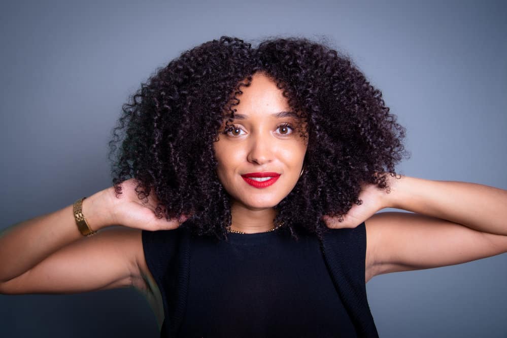 A beautiful black female with wavy hair used a leave-in conditioner and natural oils to highlight her natural texture and bring out her curly, fine hair.