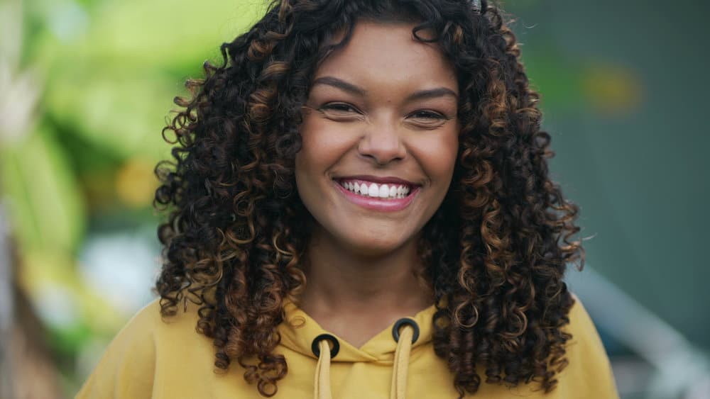 A young Brazilian girl with color-treated hair has a slightly darker hair color than most ladies with brown hair and curls styled with natural oils and a wide-tooth comb.