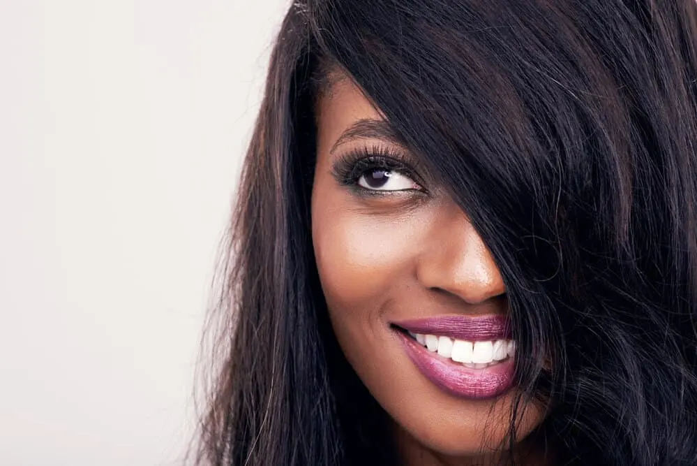 How to Part Your Hair: Part Down the Middle, to the Side & More 1 A beautiful black girl with thick hair that's wearing her hair straight with a natural part that is slightly off center on the left side of her head naturally falls around her cut face.