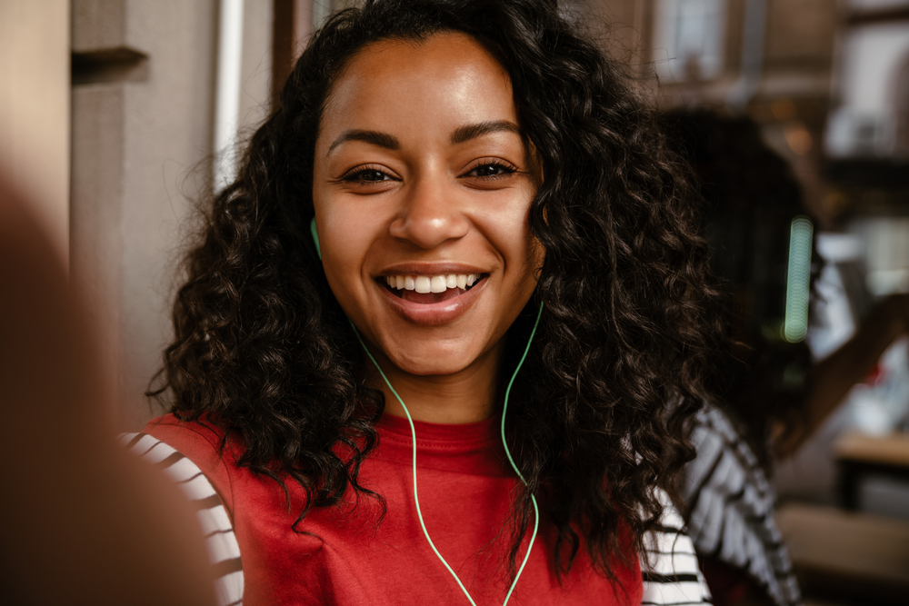 A beautiful young black woman with a 3B natural curl pattern styled with nourishing hair oil to mitigate hair breakage and smooth frizzy curls.