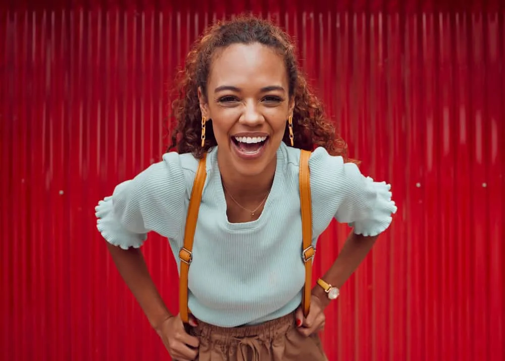 How to Take Care of Curly Hair: Hair Care Regimens for Curls 1 A cute black girl with natural curls on a type 3 hair texture styled with natural oils in a loose ponytail hairstyle that's perfect for her greasy hair.