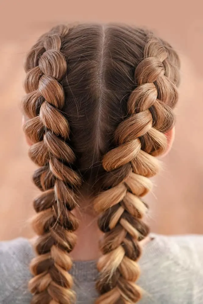 A young woman wearing inverted French braids on a type 2 hair type where each reverse French Braid uses a weaving technique that looks like a fishtail braid or waterfall braid.