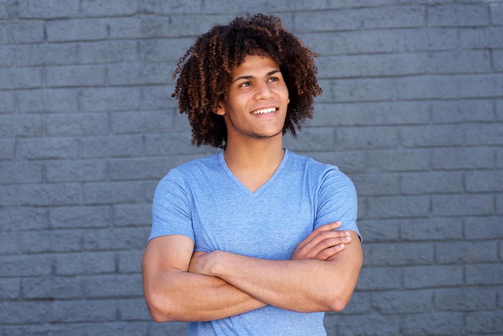 His thick, curly hair, styled in soft layers, gives an appealing contrast to the natural flow of his ombre hairstyle.