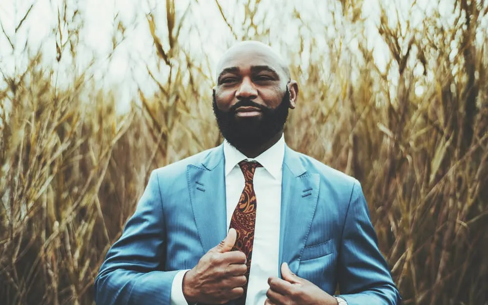 Embracing his hair's natural texture, the African man opts for a slicked-back hairstyle that draws attention to his thick, well-groomed beard.