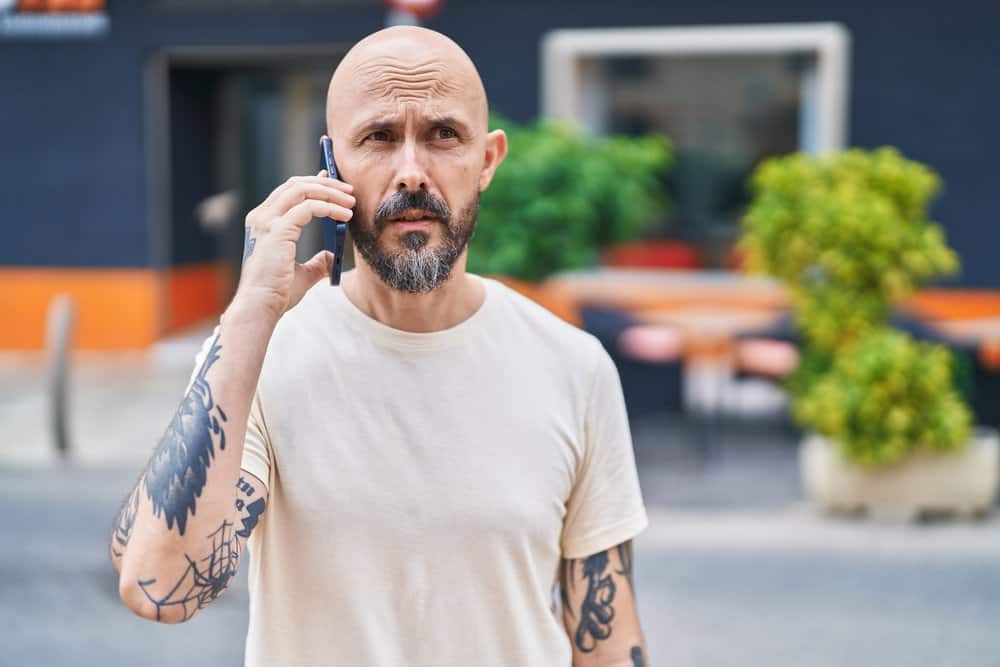 The thick, long hair on his beard complements his bald head, creating a striking contrast between his grey beard and his lack of hair on the scalp.