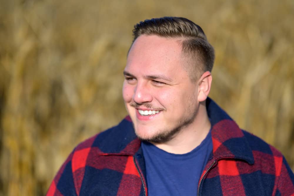 The young man's comb-over and classic fade beginning midway through his head can work on straight, curly, or wavy hair strands creating a perfect balance of edginess.