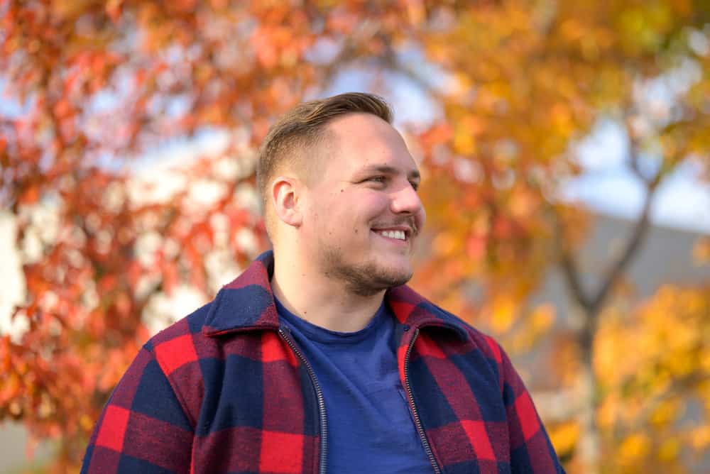 With his drop fade, tapered sides, and cool gentleman beard, the young man showcases a versatile and trendy hairstyle that complements his round face shape.