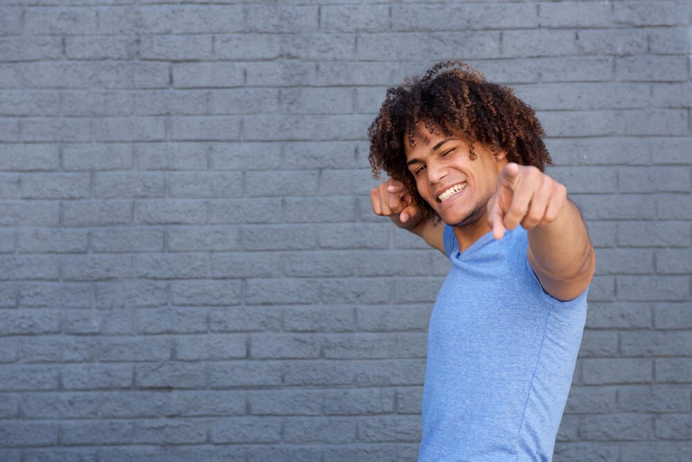 The ombre effect on the man's curly long hair elegantly transitions from dark brown at the roots to tan on the ends, embodying a laid-back style.