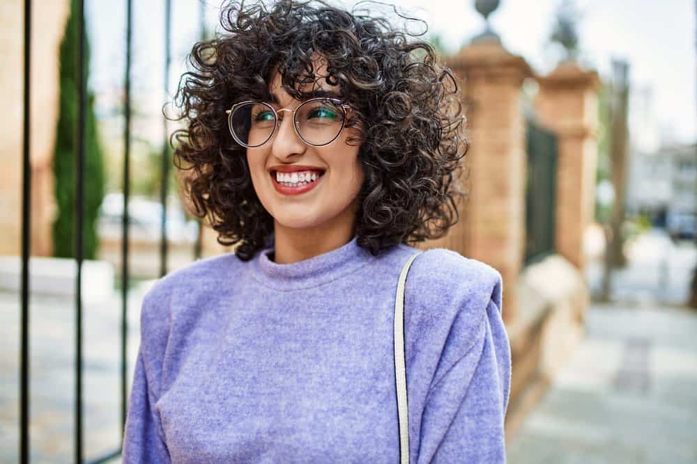 A stunning image of a young female with light-brown skin showcases her beautiful face and perfect skin, highlighted by her curly hair strands.