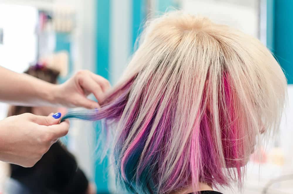 A lady with peekaboo hair dye styled with platinum blonde hair on top with a vibrant blue and bubblegum pink color underneath her naturally long hair.