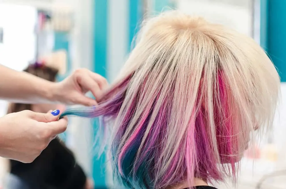 8 Underdye Hair Coloring Trends, Ideas, and Hairstyle Tips 1 A lady with peekaboo hair dye styled with platinum blonde hair on top with a vibrant blue and bubblegum pink color underneath her naturally long hair.