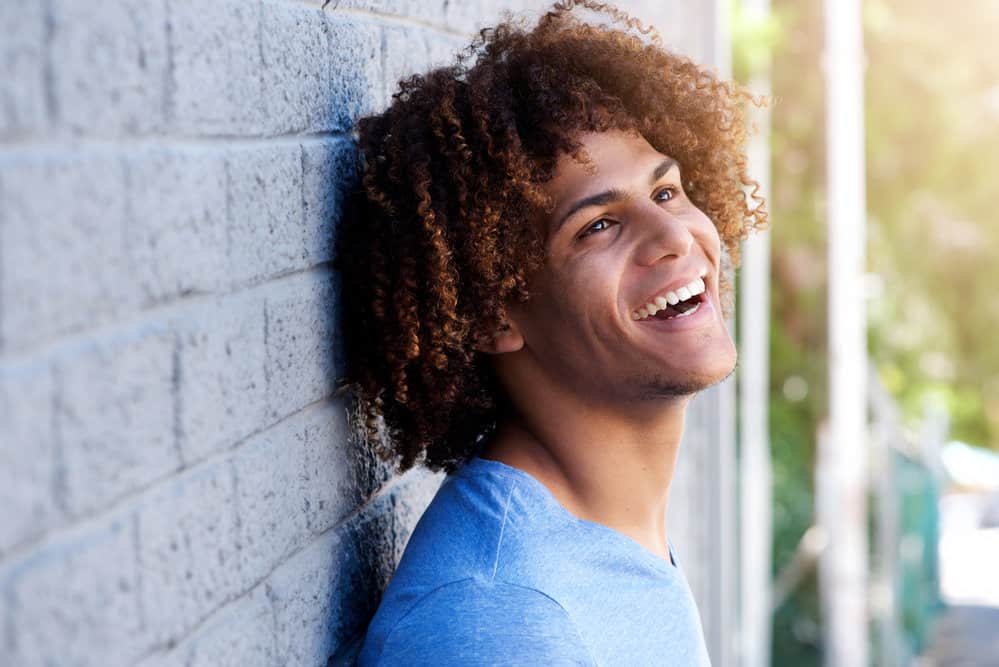 The man's hair, full of natural curls, is styled to maximize volume, creating a stunning ombre effect from dark brown to tan.