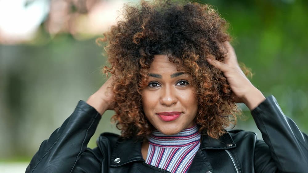 A beautiful black female with a warm skin tone showcases her hair texture and hair tone, styled with warm shades of brown and red for a natural and beautiful look.