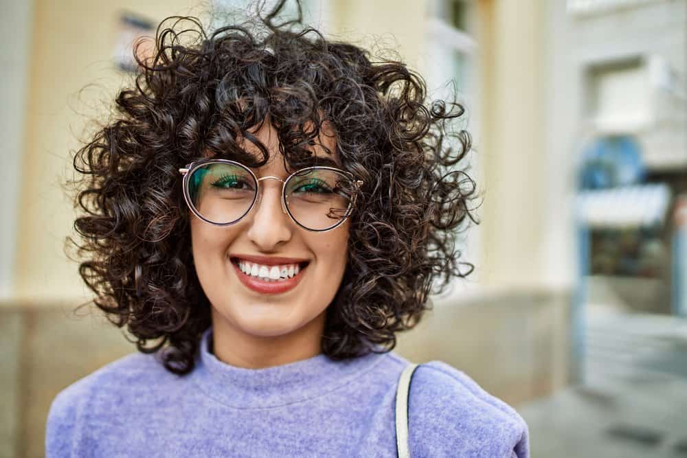 A young female with light-brown skin and curly hair bends where her straight hair was curled with a curling iron.