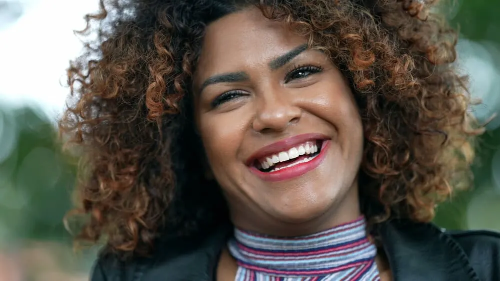 What Color Should I Dye My Hair? How to Choose a Hair Color 1 A beautiful black female with dark brown hair mixed with rose gold dyed hair strands on her reddish-brown skin tone.