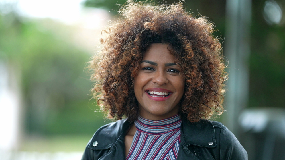 The gorgeous black female with deep skin showcases her dark chocolate hair color mixed with rose gold dyed hair strands, creating a beautiful contrast.