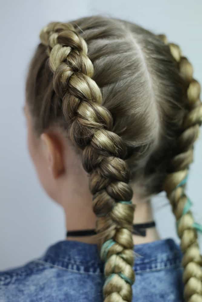 The lady's long hair is skillfully woven into intricate French braids, reflecting the cultural heritage of braided styles in West Africa with the three-strand braid.