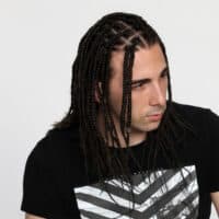 A young Caucasian male with thin braids wearing a low maintenance box braid hairstyle with a zig zag part like you would see in African culture.